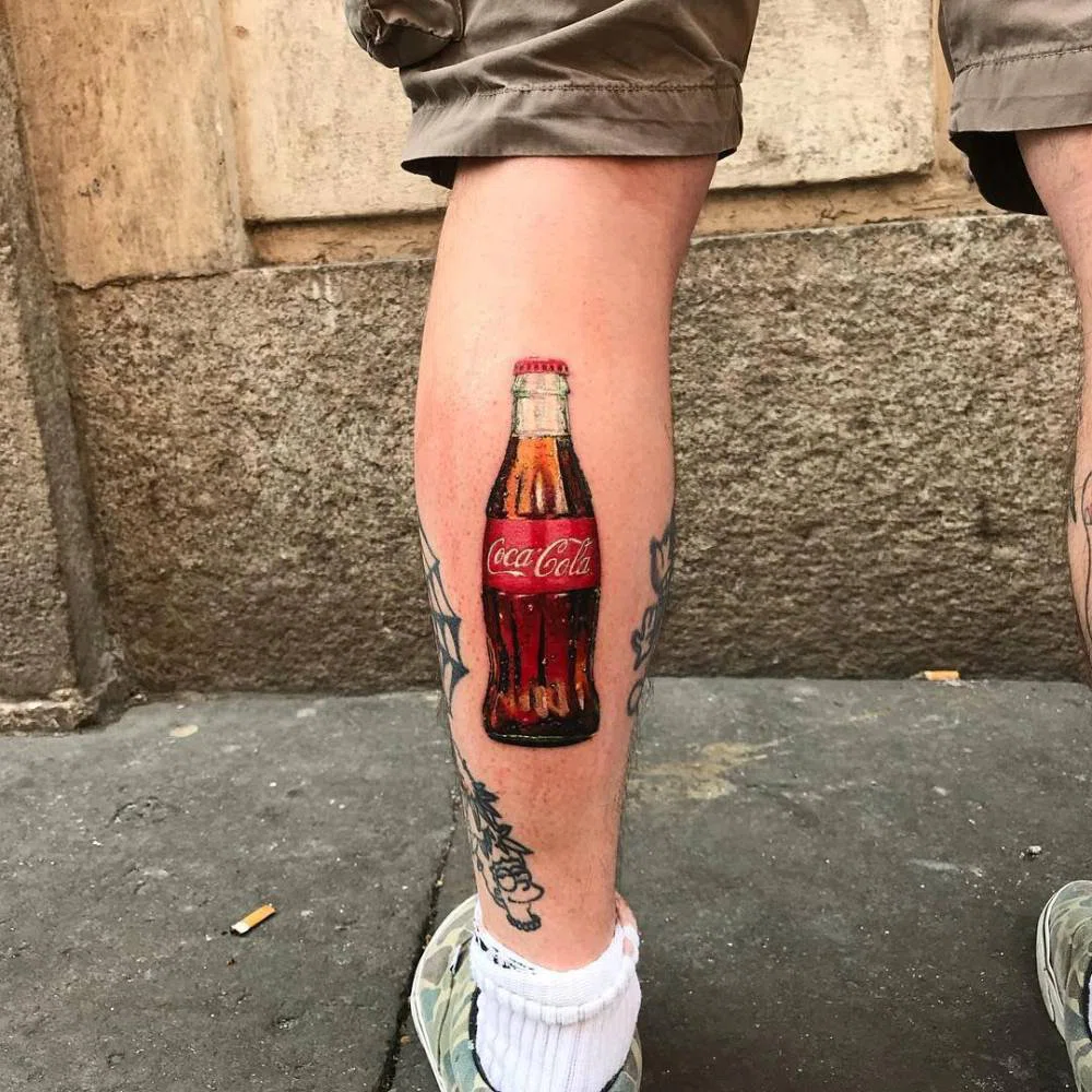 Tatuaje de una botella de cocacola en la pierna.