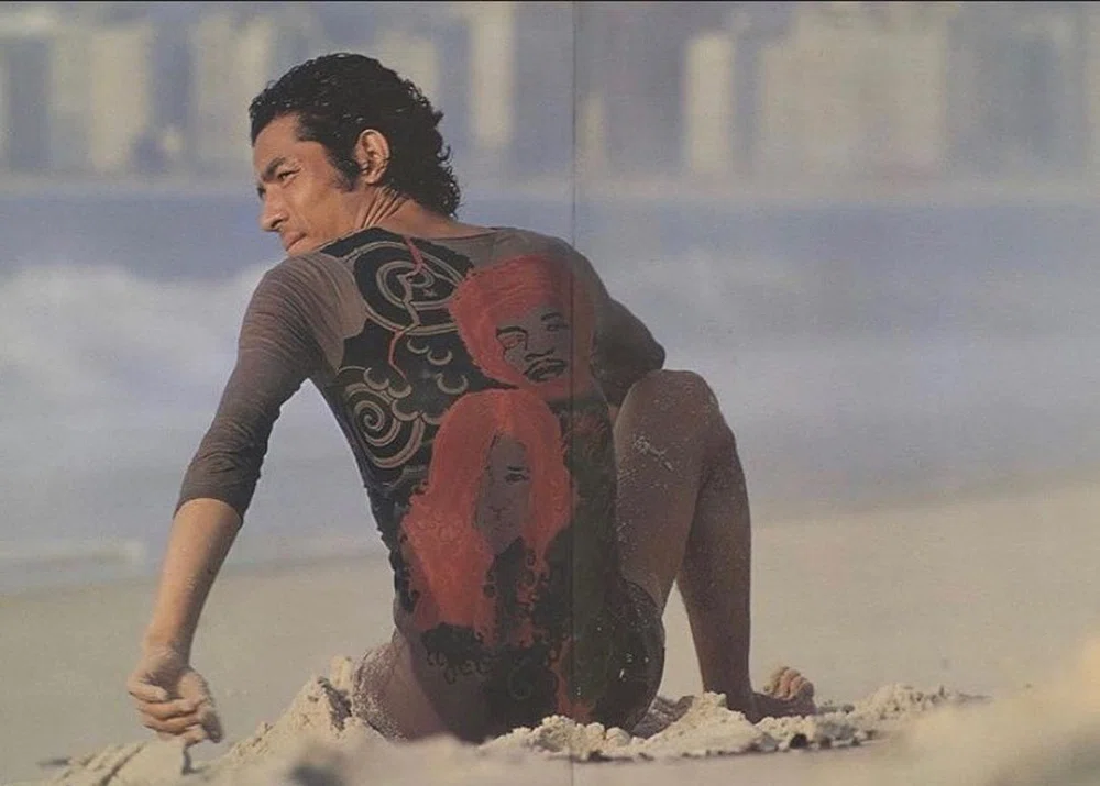 foto miyake-tatto. Hombre sentado en la playa con una licra que simula un cuerpo con tatuajes japoneses