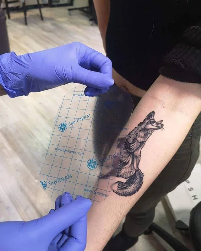 aplicando un parche dermal para cicatrizar un tatuaje en el brazo