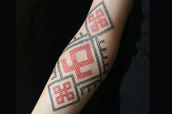tatuaje en brazo simulando un bordado en punto de cruz en colores rojo y verde.