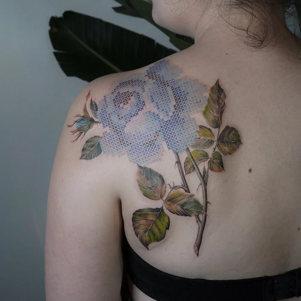 tatuaje en la espalda de una mujer de una flor mediante estilo y técnica del tatuaje bordado a punto