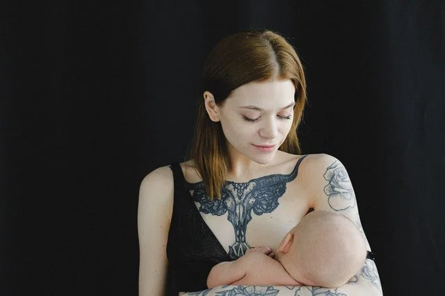 mujer dando el pecho a su hijo recien nacido con tatuajes en pecho, hombro y brazo