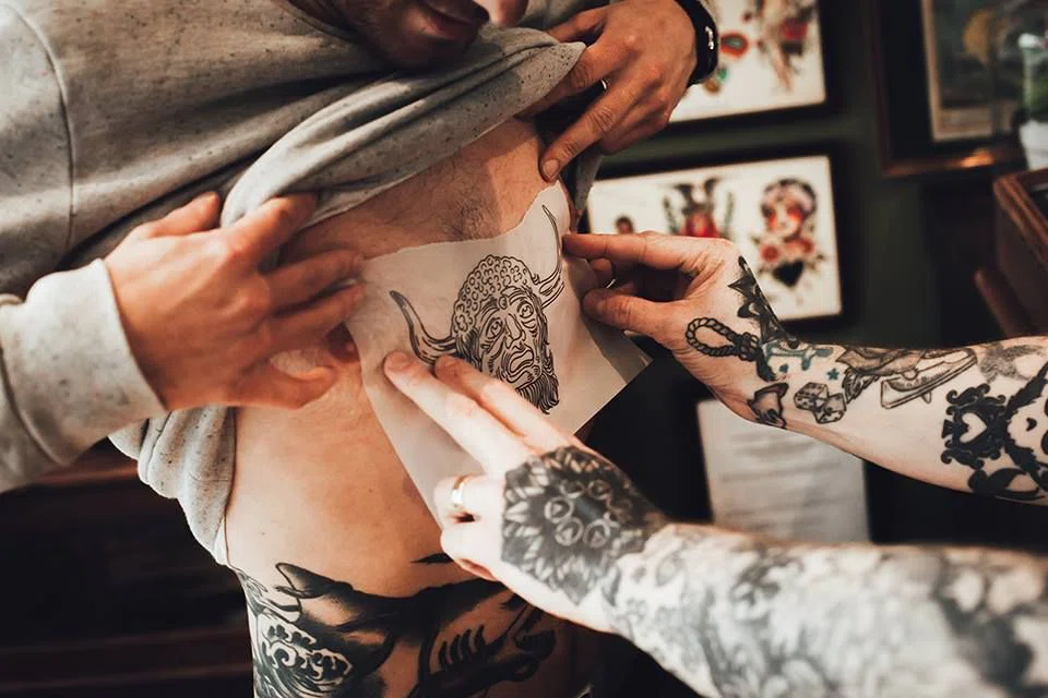 Aplicando esténcil en el cuerpo antes de tatuar. Plantilla que lleva impreso el diseño que se va a tatuar